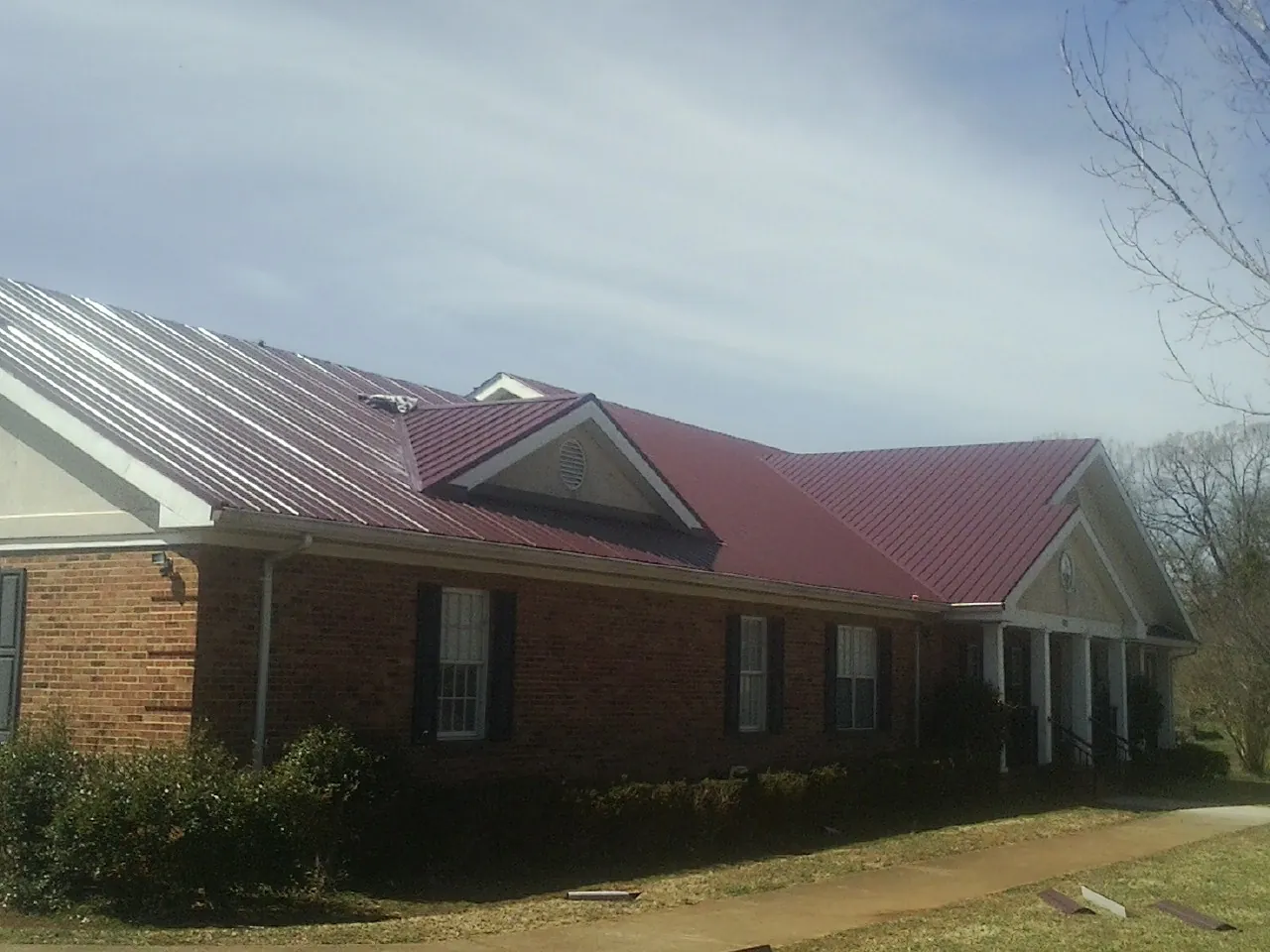 Red metal roof with gabled entries on a long brick building, from a Hail Damage Roof Repair job in Whiteville