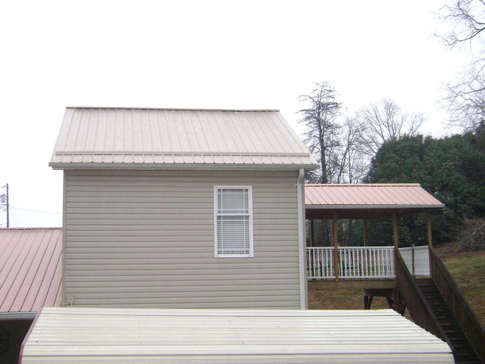 Tan metal roofs on a two story addition and attached porch, from a Roof Replacement job in Whiteville